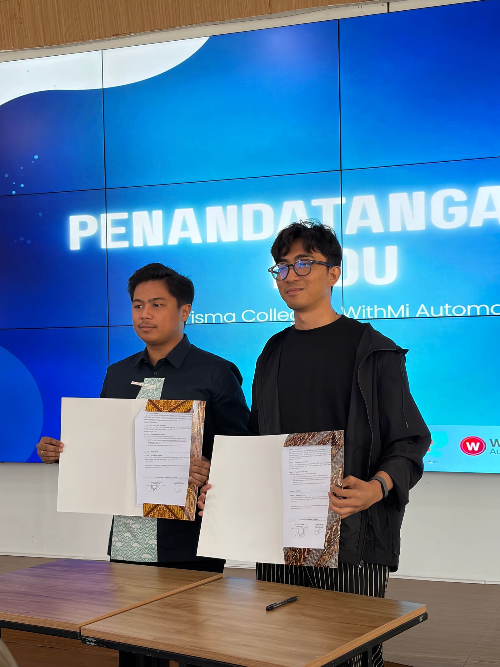 Penandatanganan MoU antara KHARISMA College dan WithMi Automation, dua penanda tangan memegang dokumen yang sudah ditandatangani