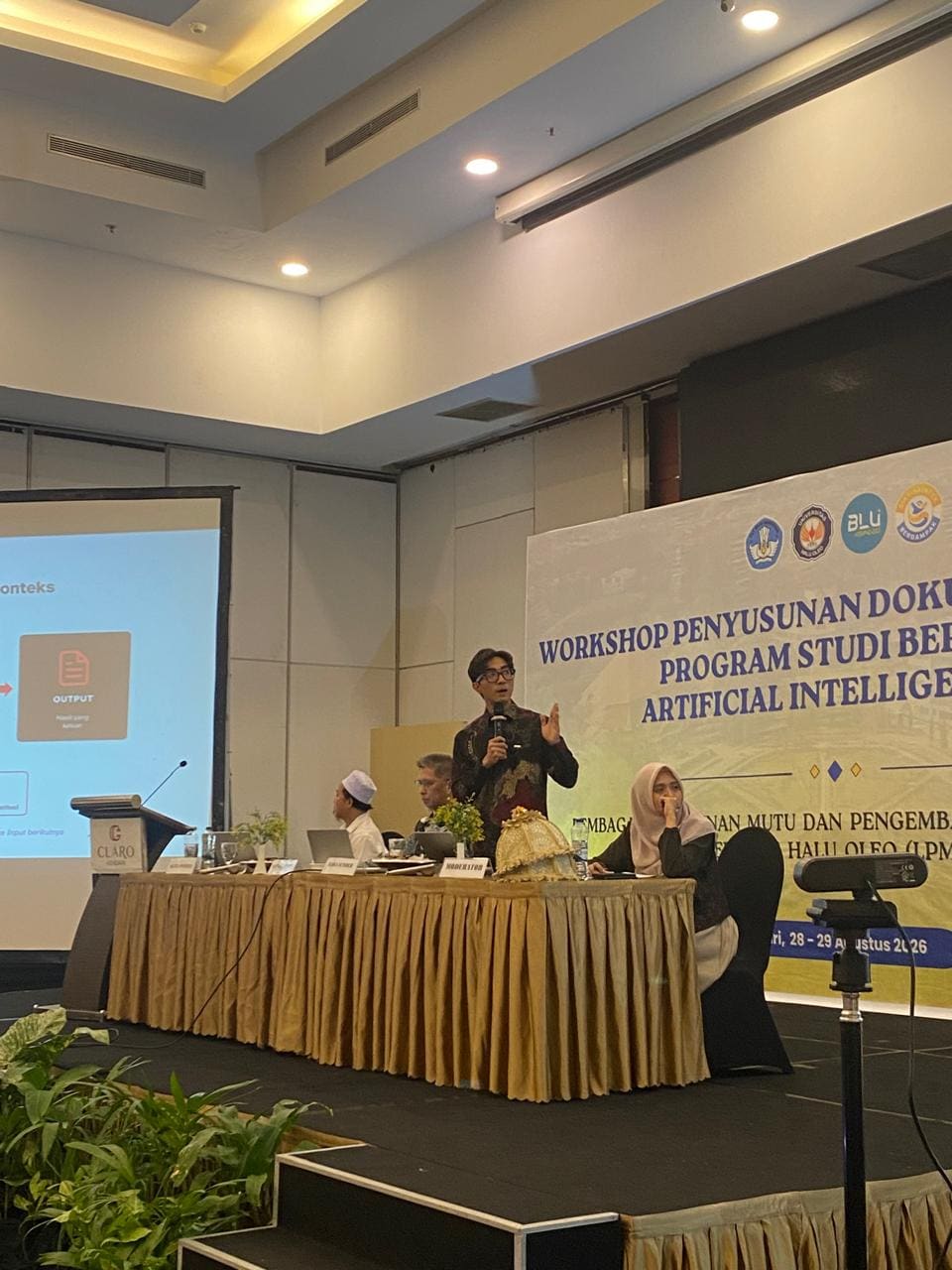 Fahmi Fahreza explaining the material at Universitas Halu Oleo with a microphone, the input-to-output workflow slide on screen