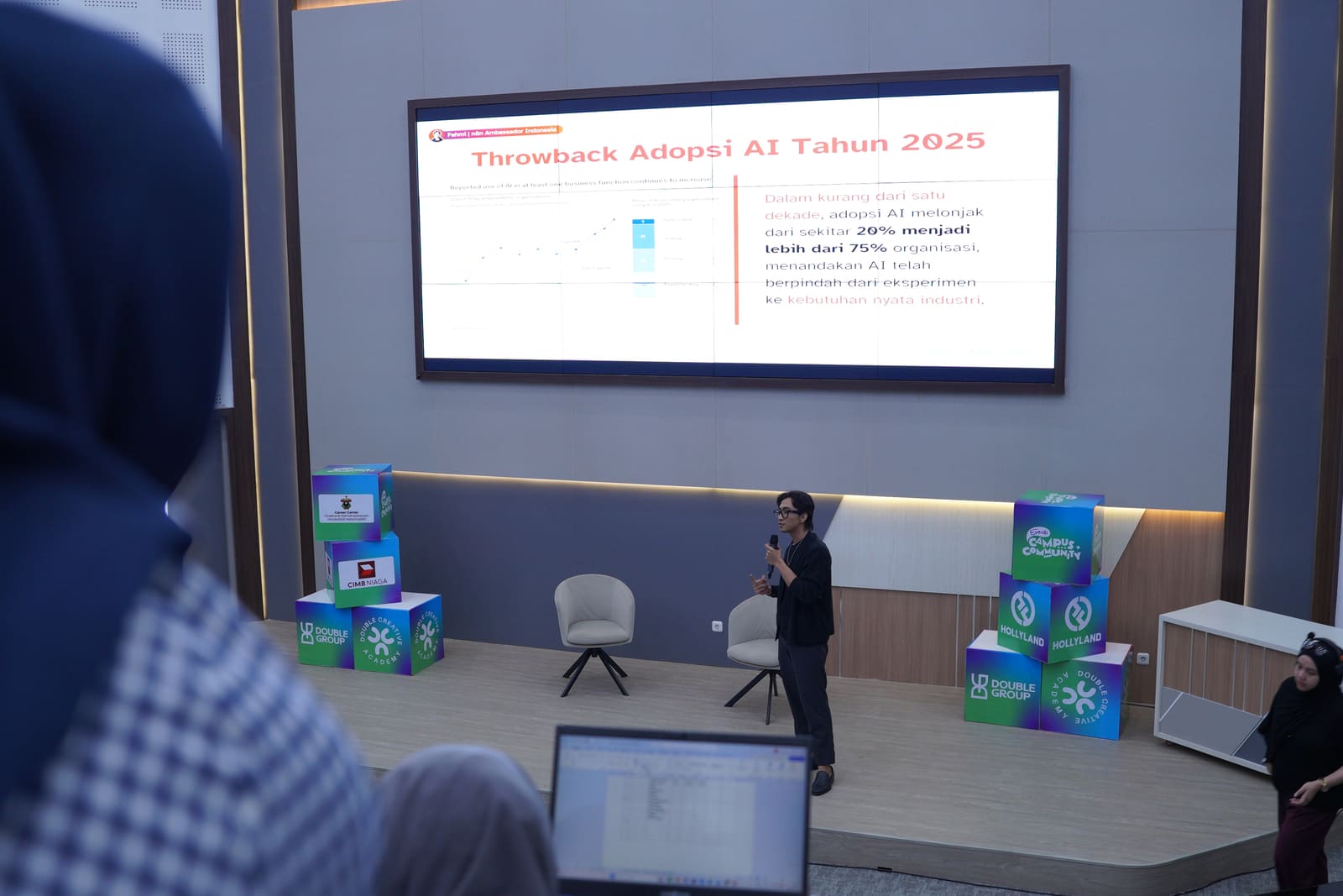 Fahmi Fahreza delivering the Campus Community session at Universitas Hasanuddin, an AI adoption slide on the large stage screen
